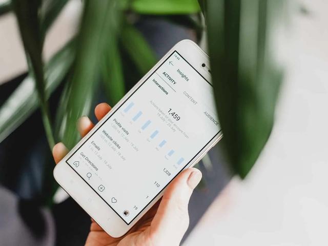 A hand holds a phone showing Instagram Insights, with a bar chart and profile visit stats