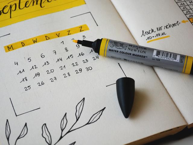 A hand-drawn September calendar in a notebook with a yellow watercolor marker resting on top