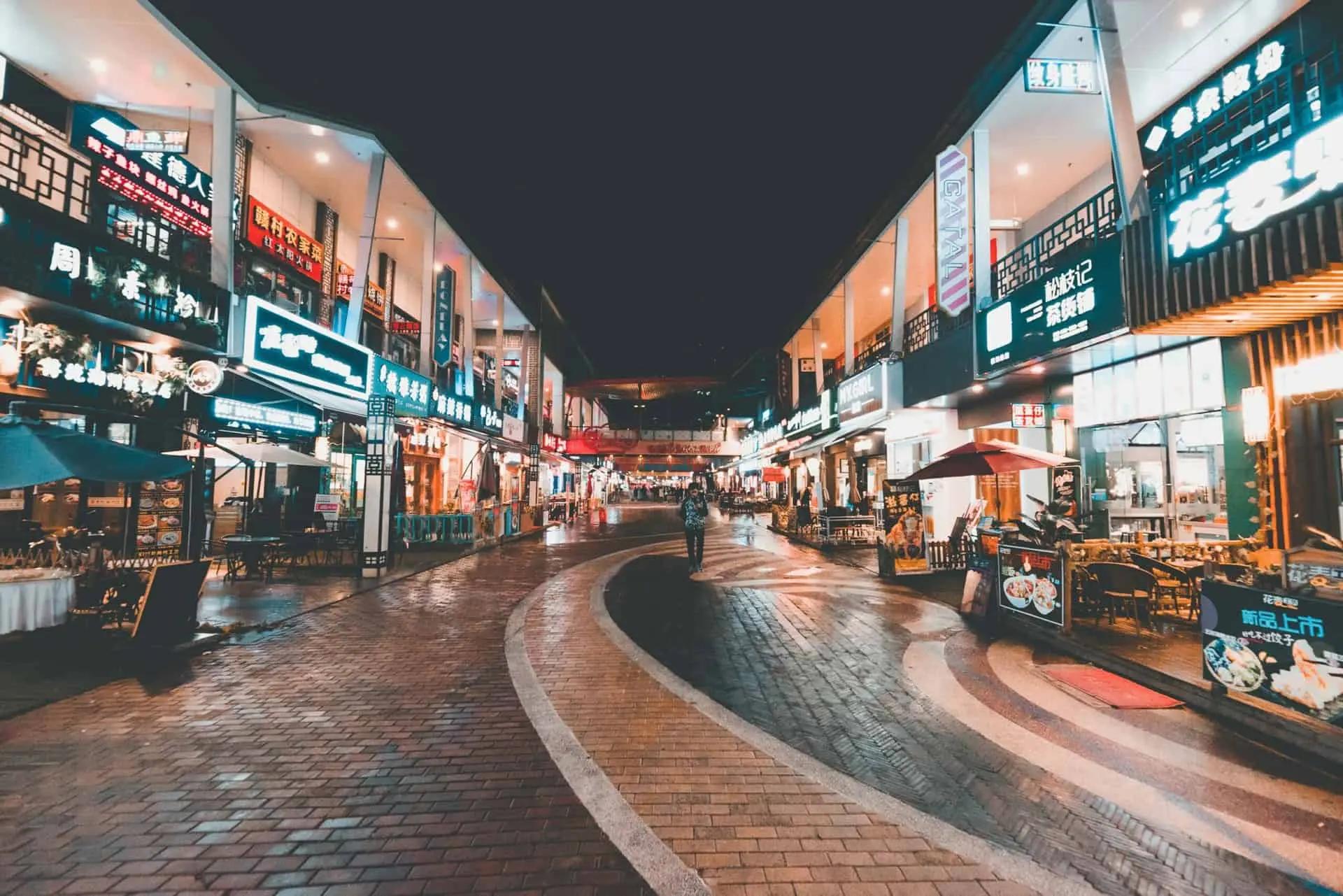 A row of illuminated shopfronts with neon signs lining a paved pedestrian street at night