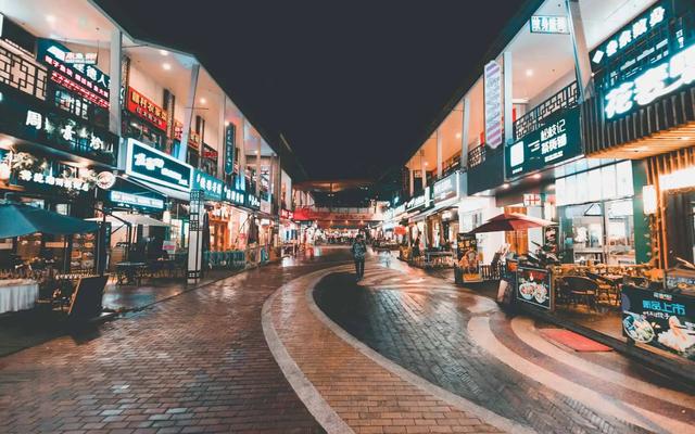 A row of illuminated shopfronts with neon signs lining a paved pedestrian street at night