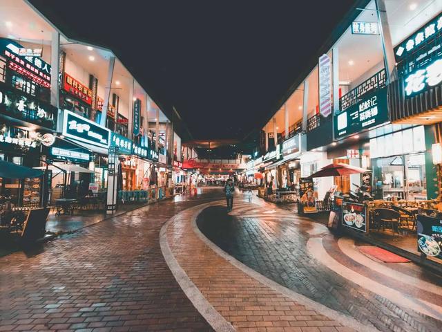 A row of illuminated shopfronts with neon signs lining a paved pedestrian street at night