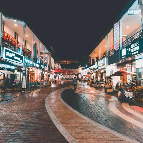 A row of illuminated shopfronts with neon signs lining a paved pedestrian street at night