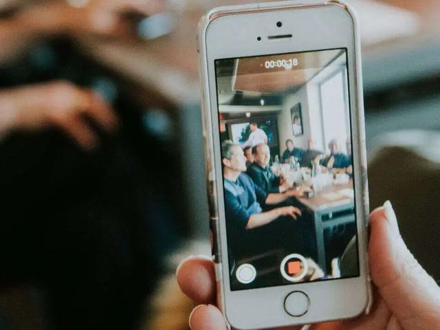 Una mano sostiene un teléfono grabando un video de personas sentadas en una mesa de restaurante