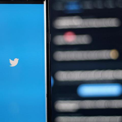 Un smartphone con el logo del pájaro de Twitter en pantalla azul, con un feed desenfocado de fondo.