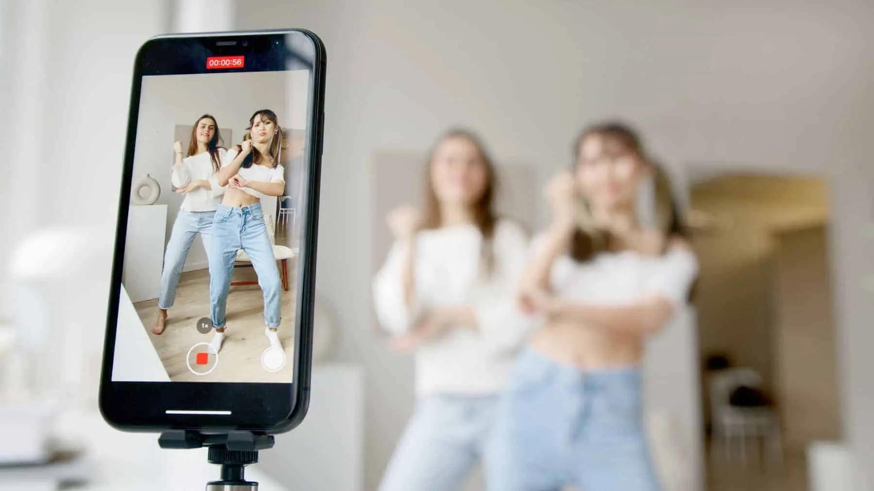 Un telefono en un tripode grabando a dos mujeres bailando una coreografia