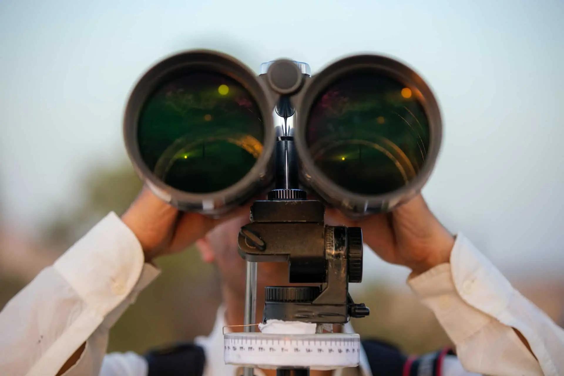 Close-up of a person looking through large tripod-mounted binoculars