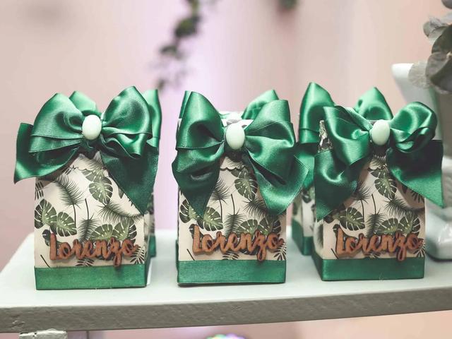 Several small gift boxes with green satin bows, tropical leaf patterns, and wooden cutouts spelling "Lorenzo"