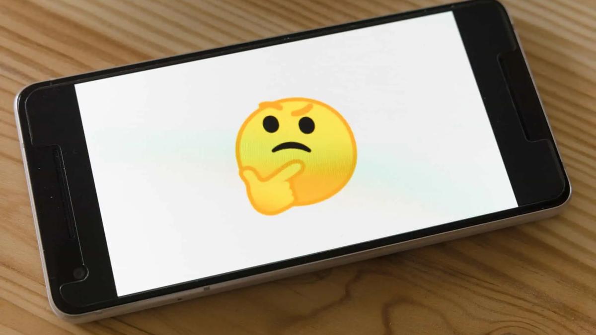 A smartphone lying on a wooden table displaying a large thinking-face emoji on screen