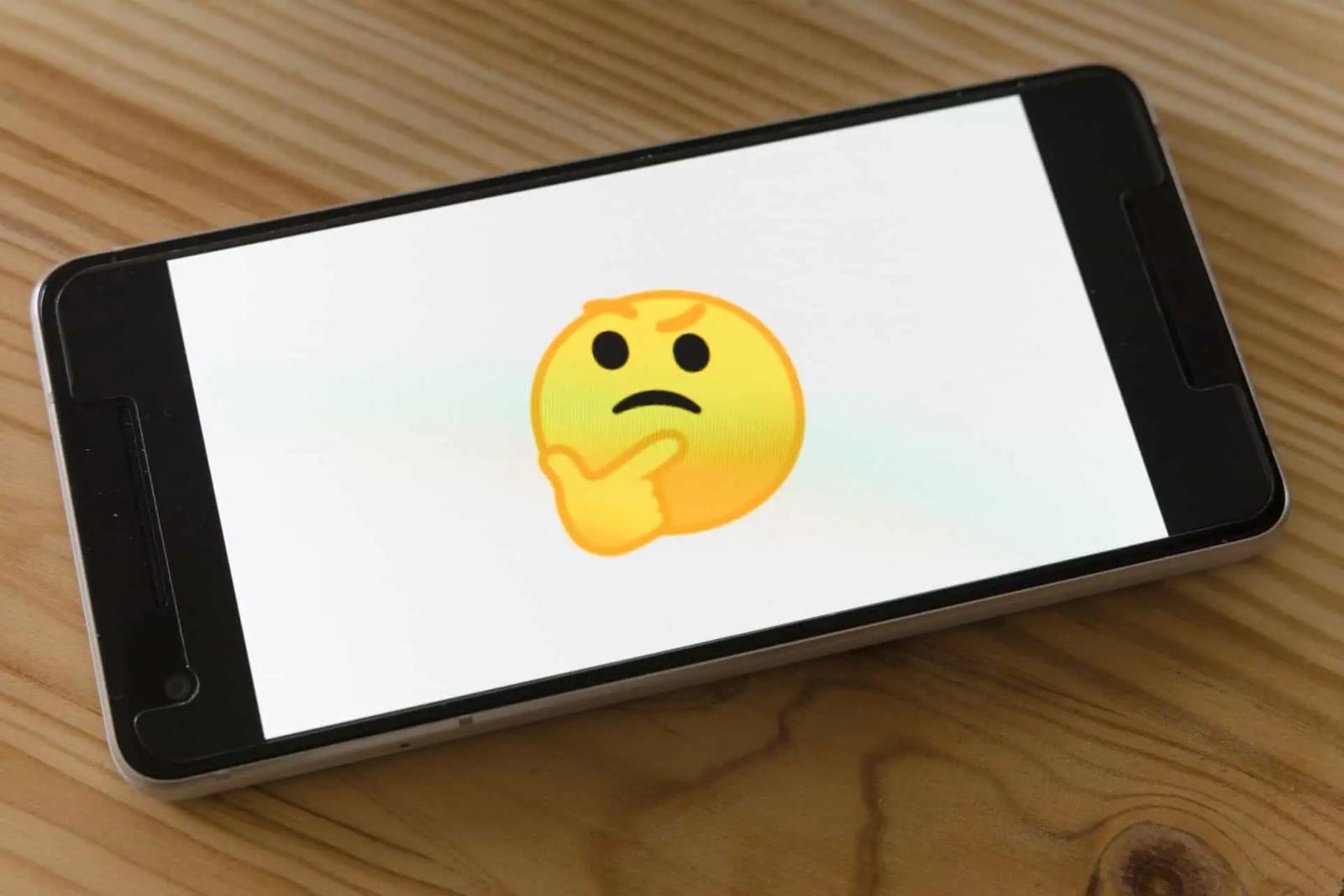 Un smartphone sobre una mesa de madera con un emoji de cara pensativa en la pantalla