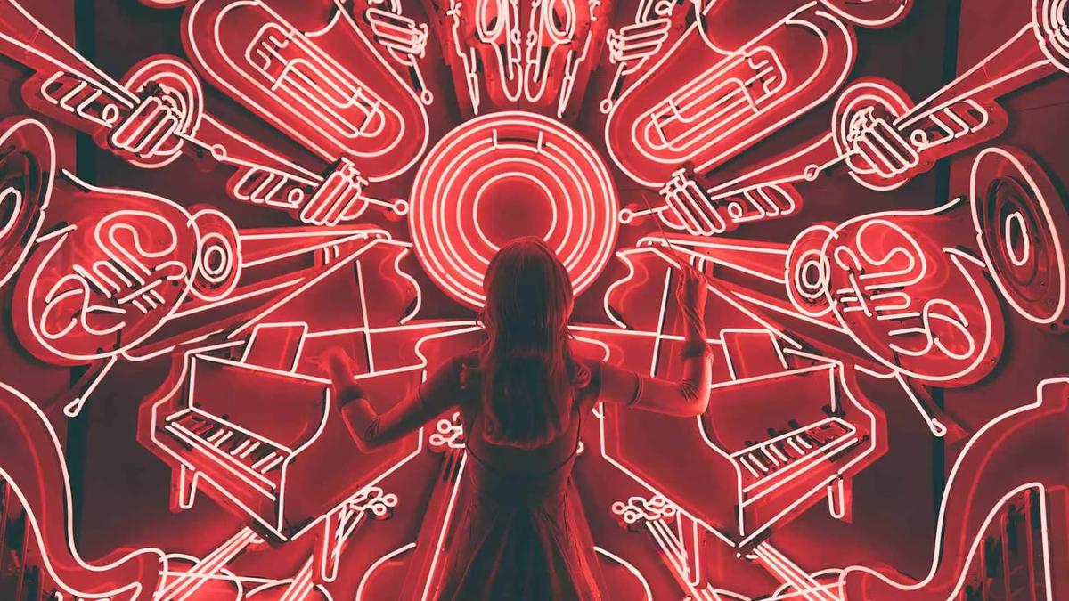 A woman stands before a symmetrical red neon display of musical instruments like pianos and horns