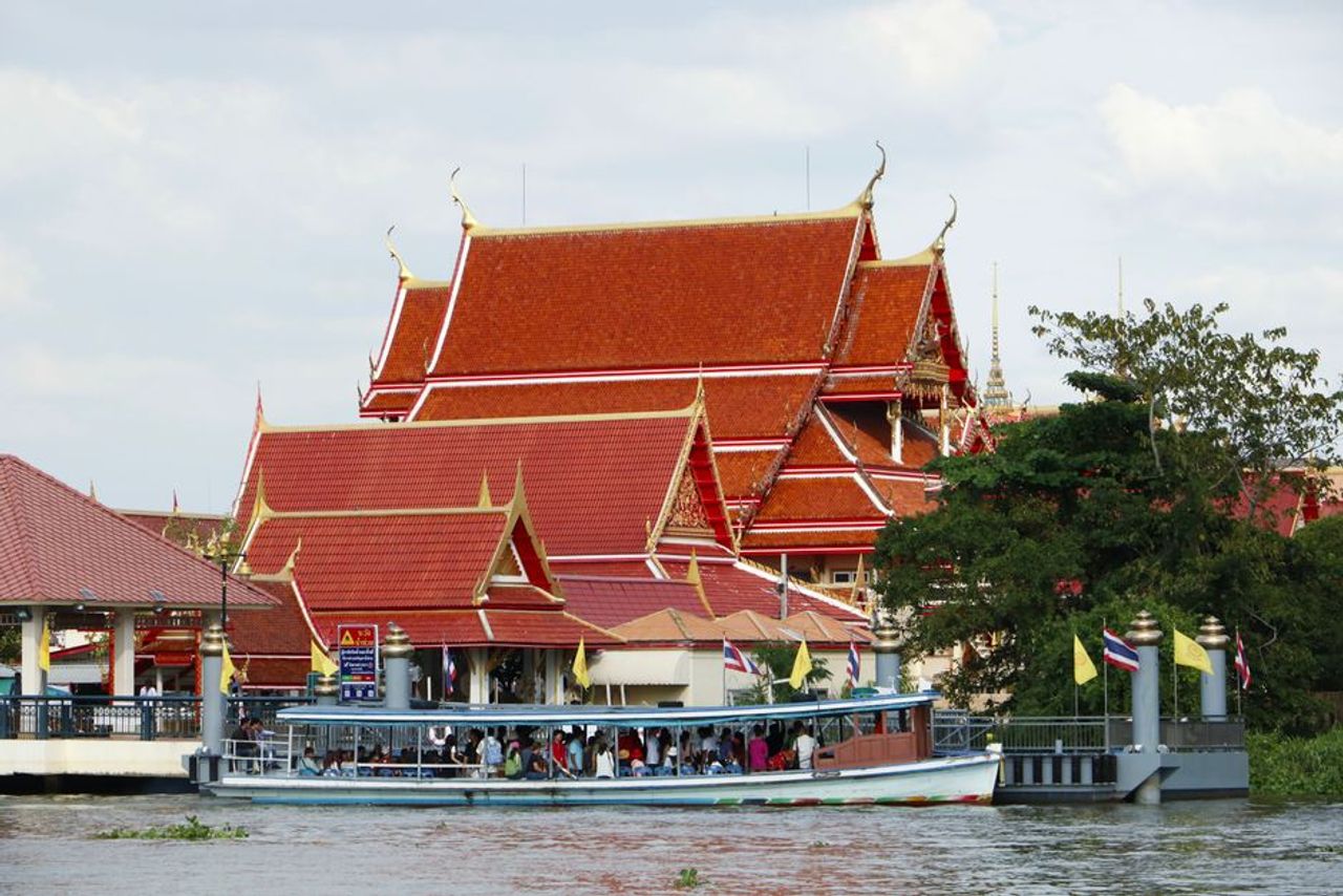 A Chao Phraya Express Boat passing a temple on the river in Bangkok
