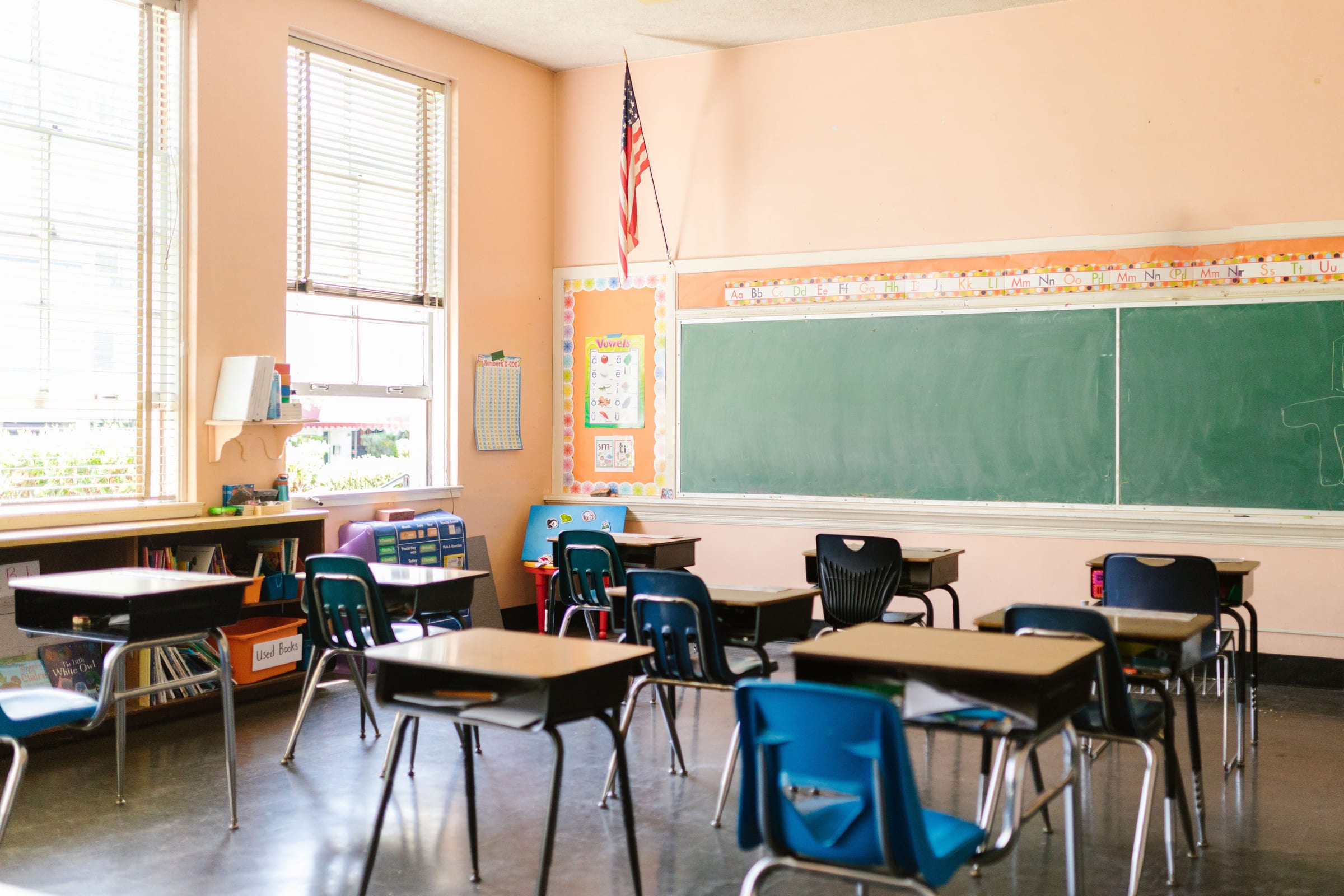 An empty classroom with rows of desks facing a green chalkboard