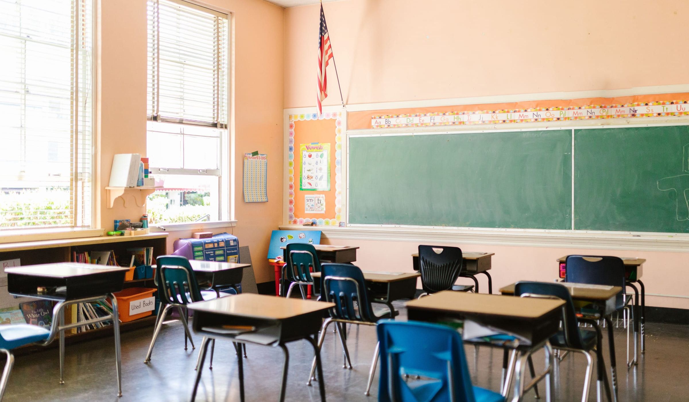An empty classroom with rows of desks facing a green chalkboard