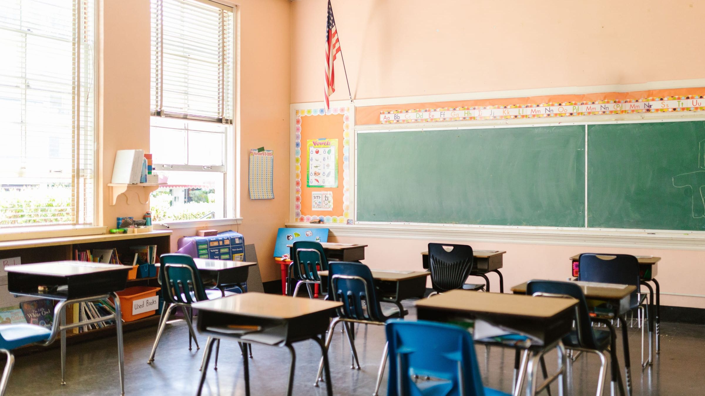 An empty classroom with rows of desks facing a green chalkboard