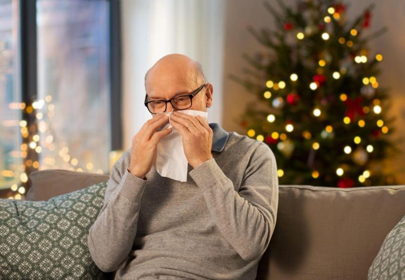 Man blowing his nose in front of a Christmas tree.