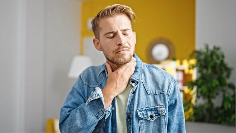 A man holding his throat grimacing slightly