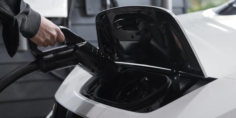 En hvit elbil som kobles til en elbil-lader.