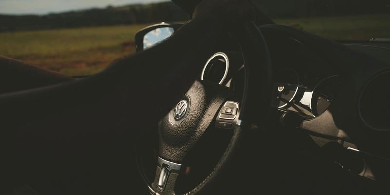 Person som holder hånden på rattet til en mørk bil som kjører ned en landevei.