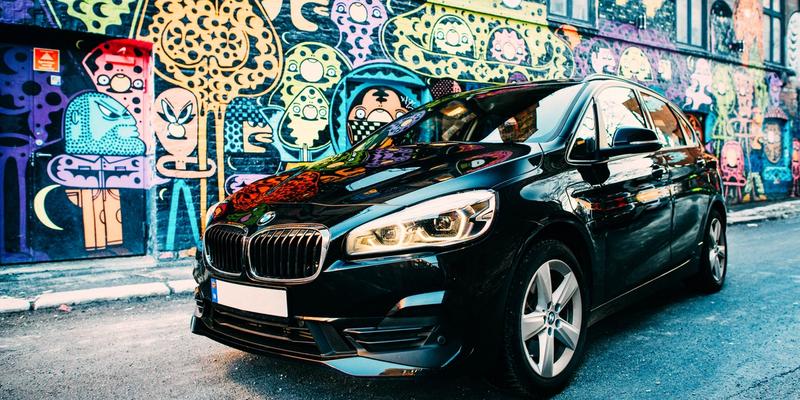 En svart bil foran en fargerik grafittivegg.