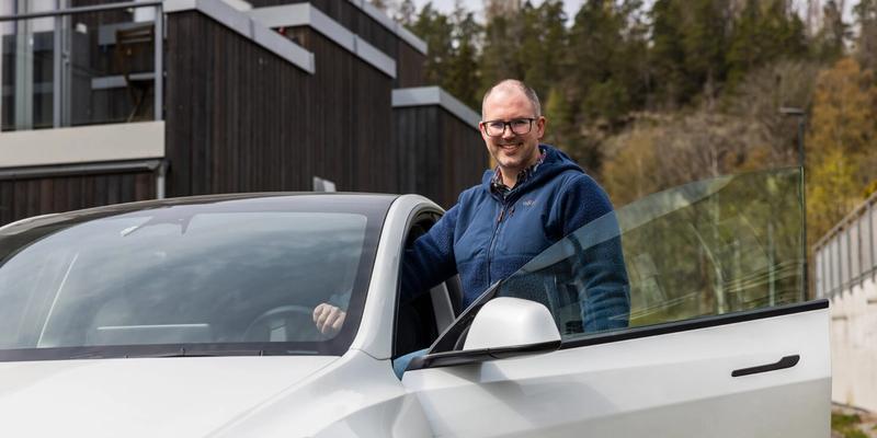 En mann som smiler i kamera mens han står med bilen sin og har bildøra åpen.