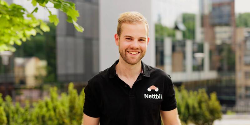 En mann som smiler mot kamera i svart pique og med grønne planter bak
