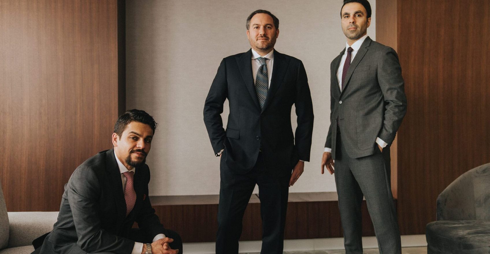 Three lawyers in suits photographed in a wood-panelled boardroom