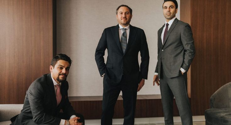 Three lawyers in suits photographed in a wood-panelled boardroom