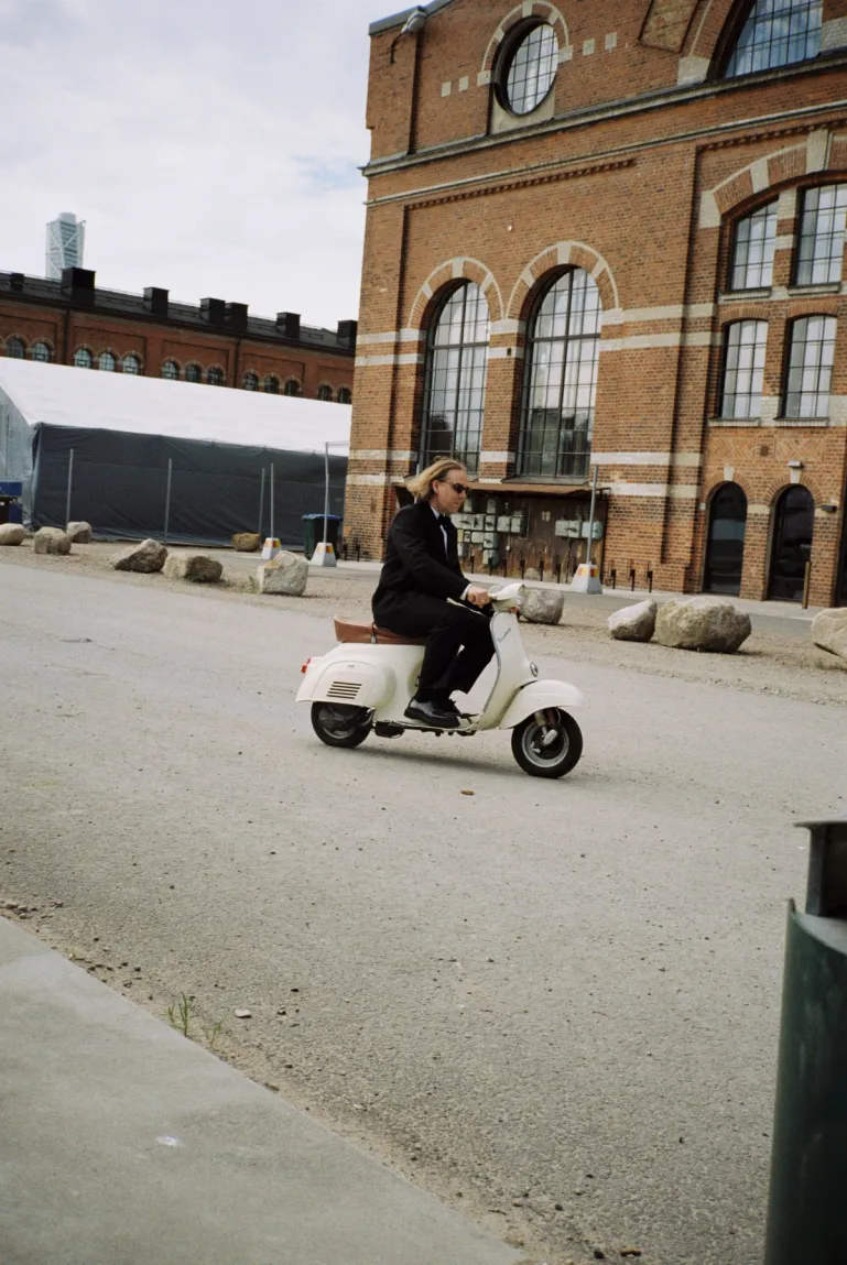 man driving a white vespa in a suit