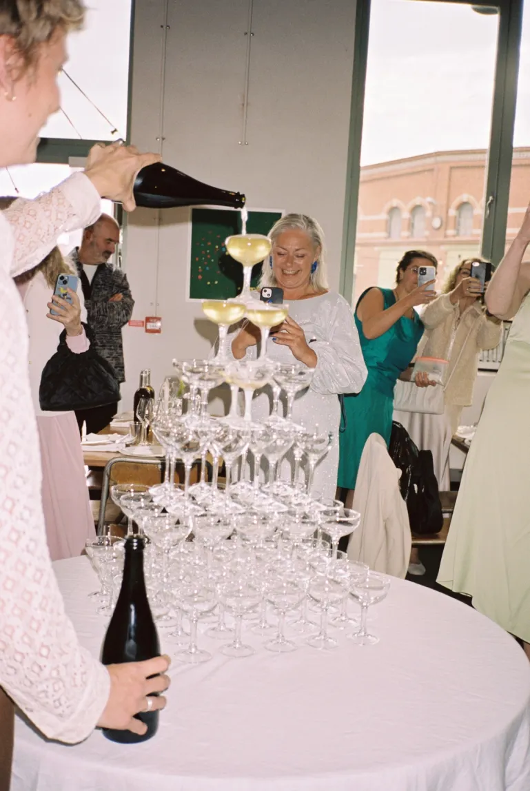 waiter pouring sparkling wine in a champagne tower with guests around the table looking