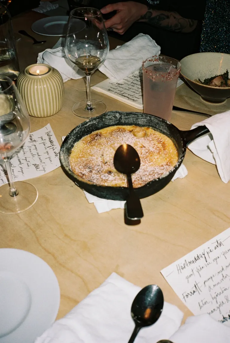 table setting with handwritten menu, a cast iron skillet with a cake, wine glasses, a candle and a paloma cocktail