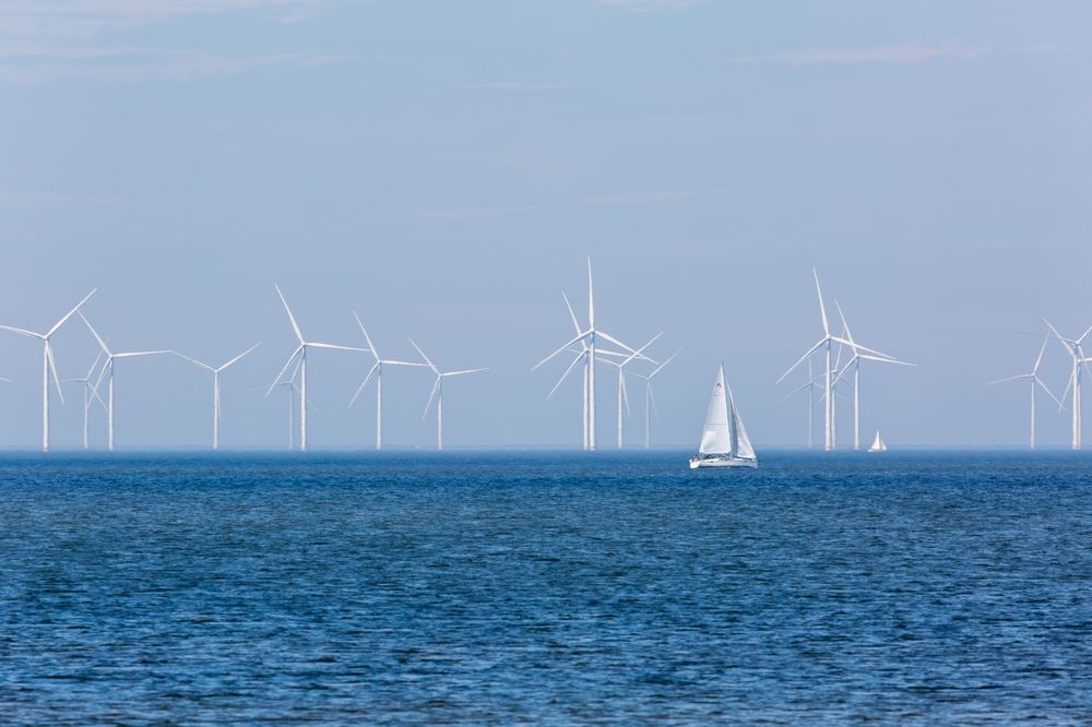 Offshore wind turbines on the horizon behind a sailboat, representing the U.S. Wind dispute affecting Ocean City and Maryland.