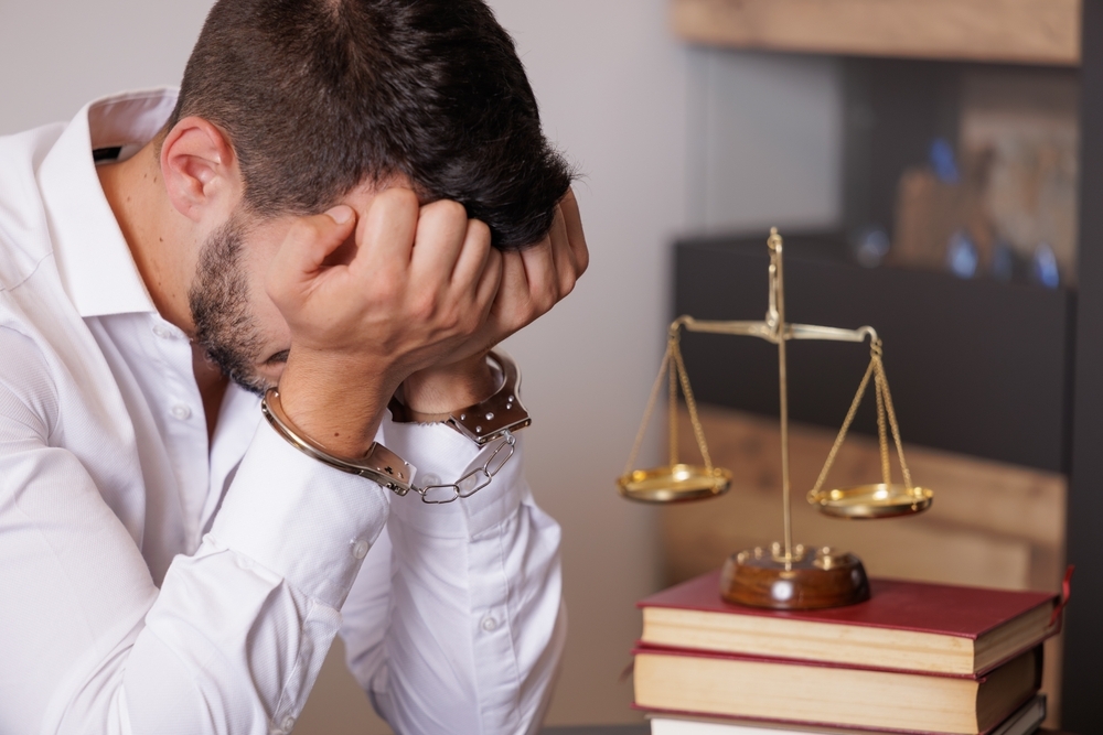 Image Man in handcuffs with head down beside law books and scales of justice, representing the fear of jail after a first-time DUI arrest in Maryland