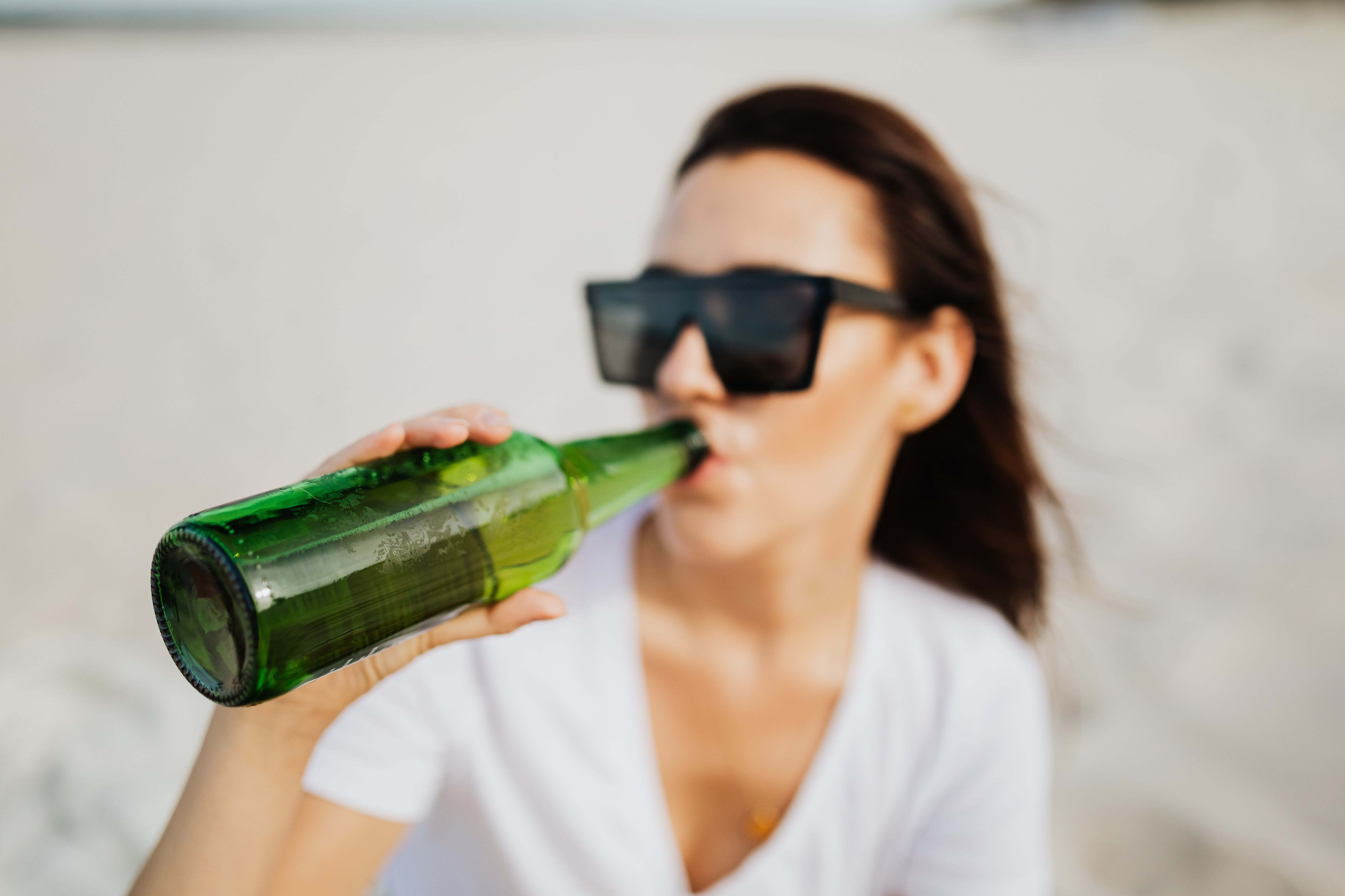 Woman in sunglasses drinking from a green beer bottle on an Ocean City beach during a Fourth of July vacation
