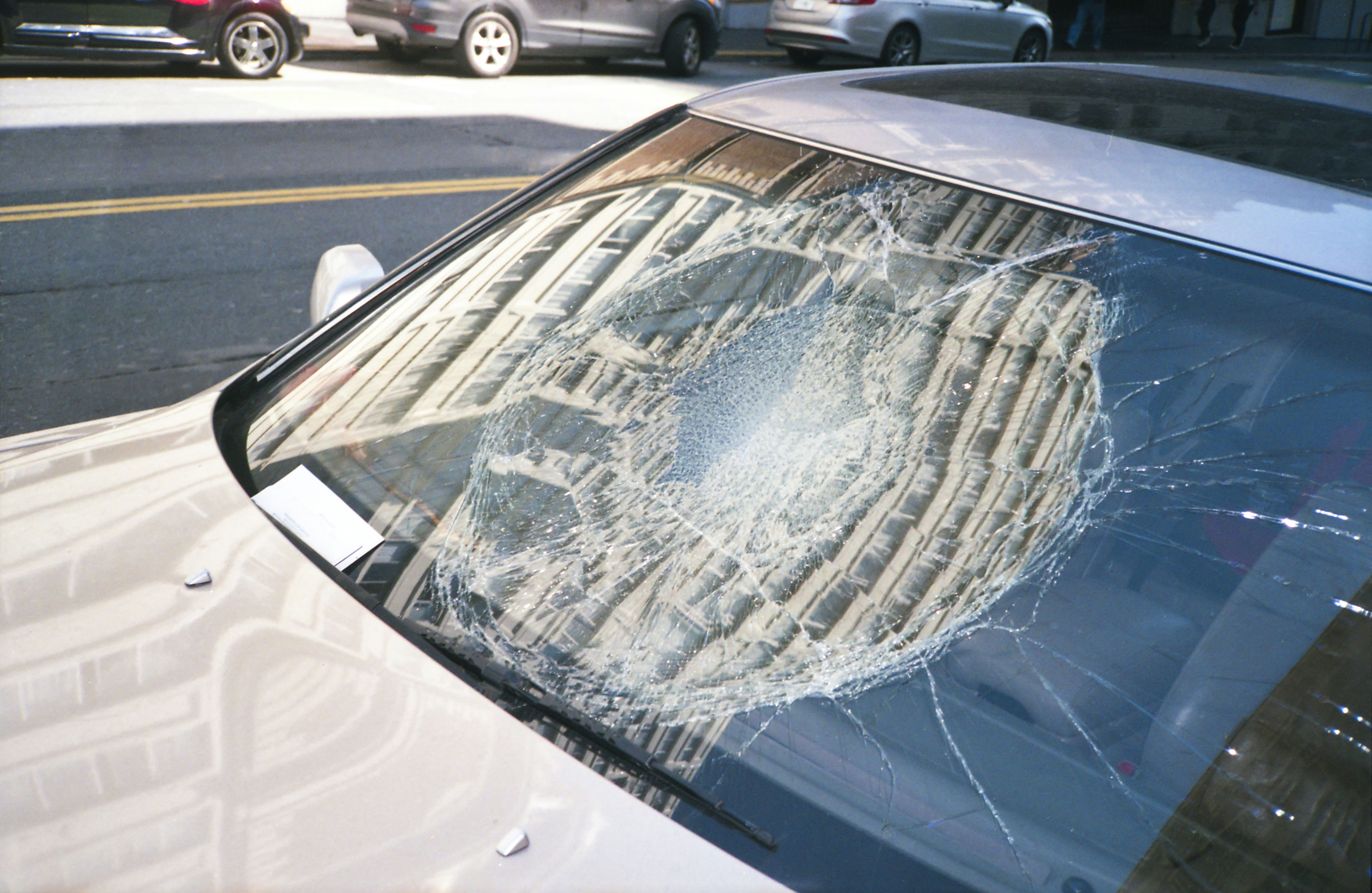 Severely cracked car windshield showing impact damage after a collision on a busy street