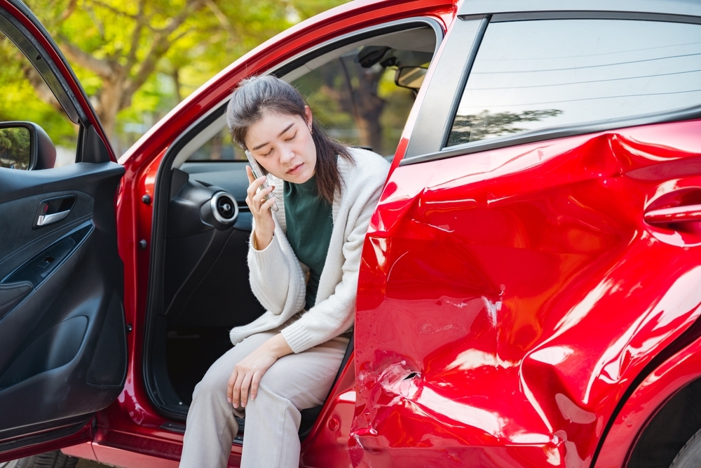 Image Woman sitting in damaged red car after Ocean City crash speaking on phone about car accident injury claim in Maryland