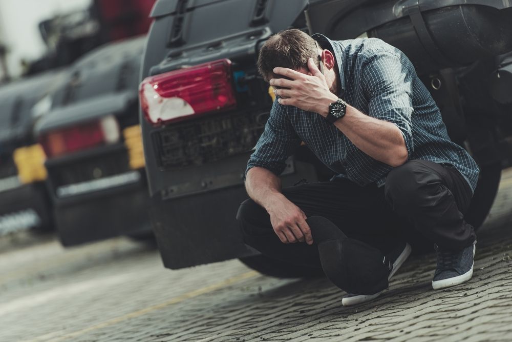 A man in distress sitting by a vehicle, representing the long-term stress of wondering how long a DUI stay on record will impact his future and Maryland criminal history.