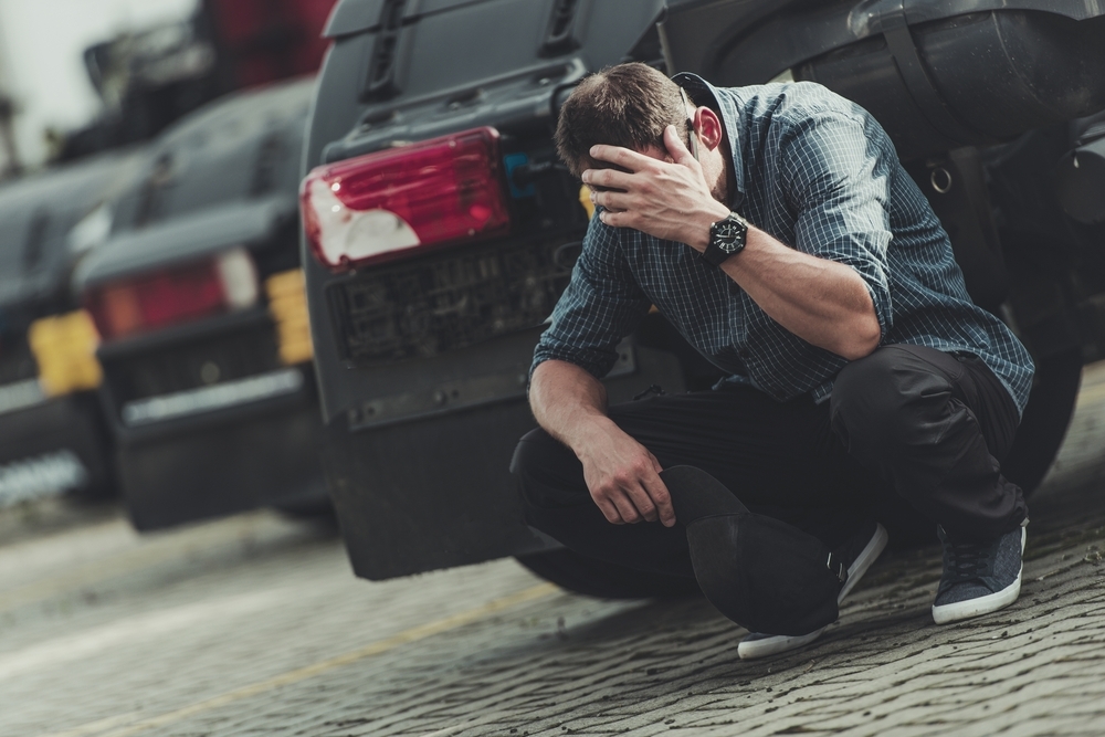 Image A man in distress sitting by a vehicle, representing the long-term stress of wondering how long a DUI stay on record will impact his future and Maryland criminal history.