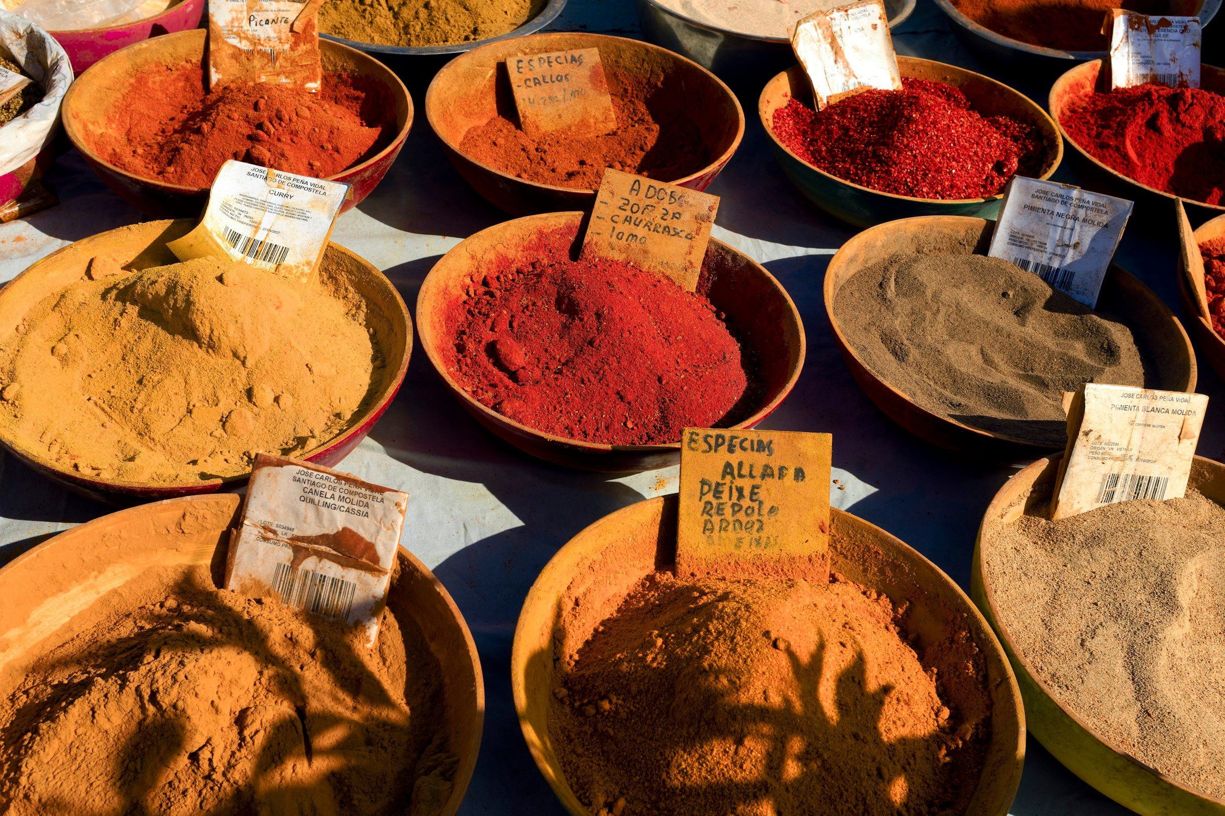 Bowls of coloured spices and powders on a market table.