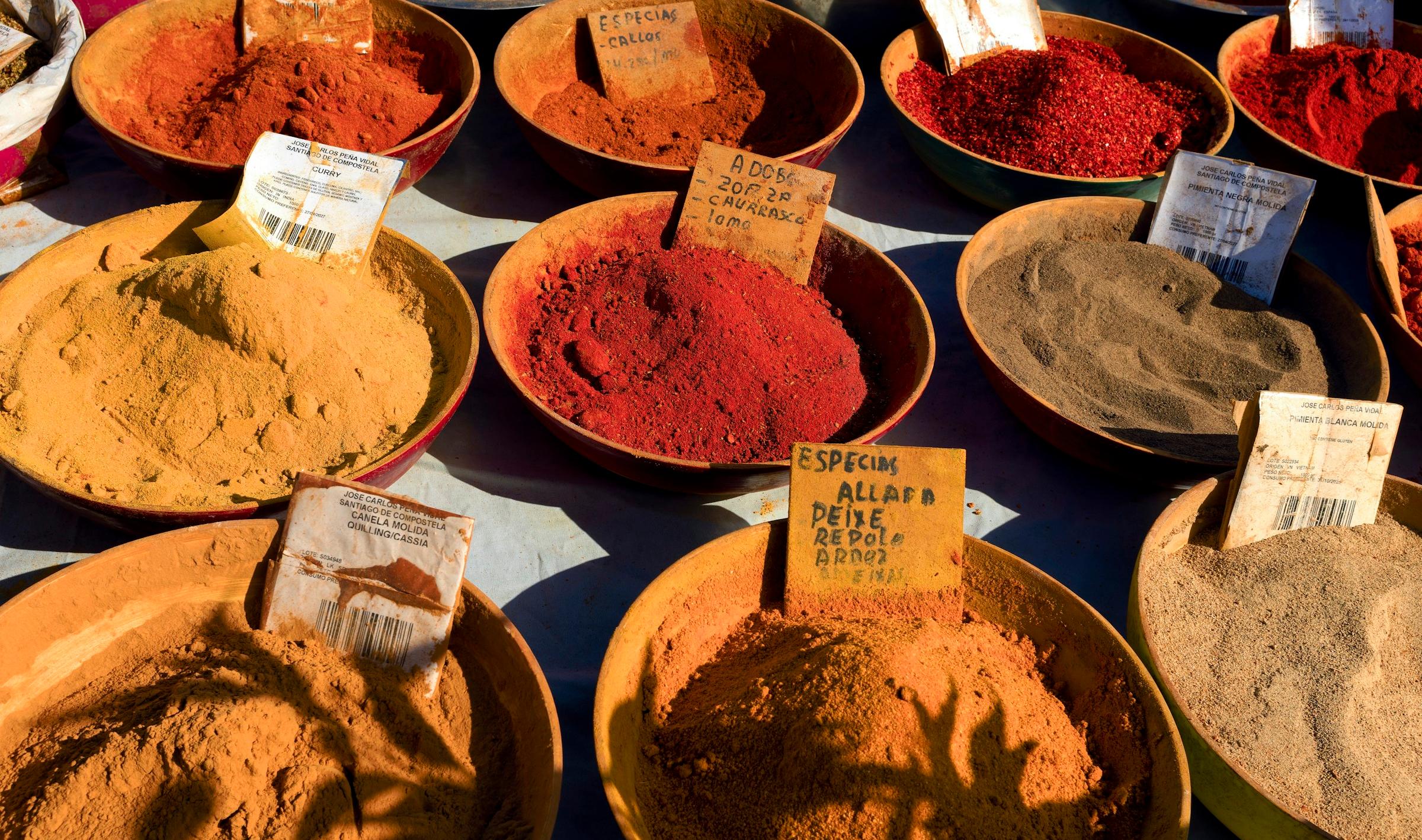 Bowls of coloured spices and powders on a market table.
