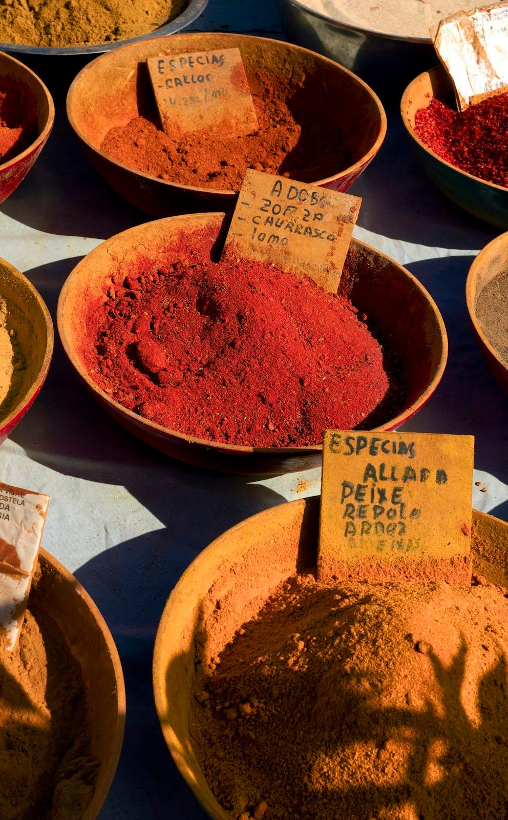 Bowls of coloured spices and powders on a market table.