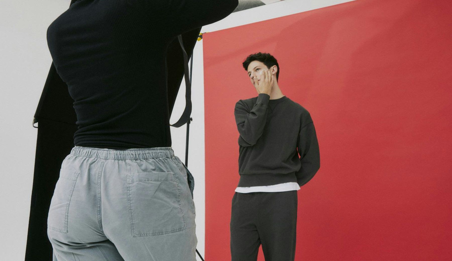 A model in grey and black standing against a red backdrop, seen past the shoulder of the photographer in the foreground.