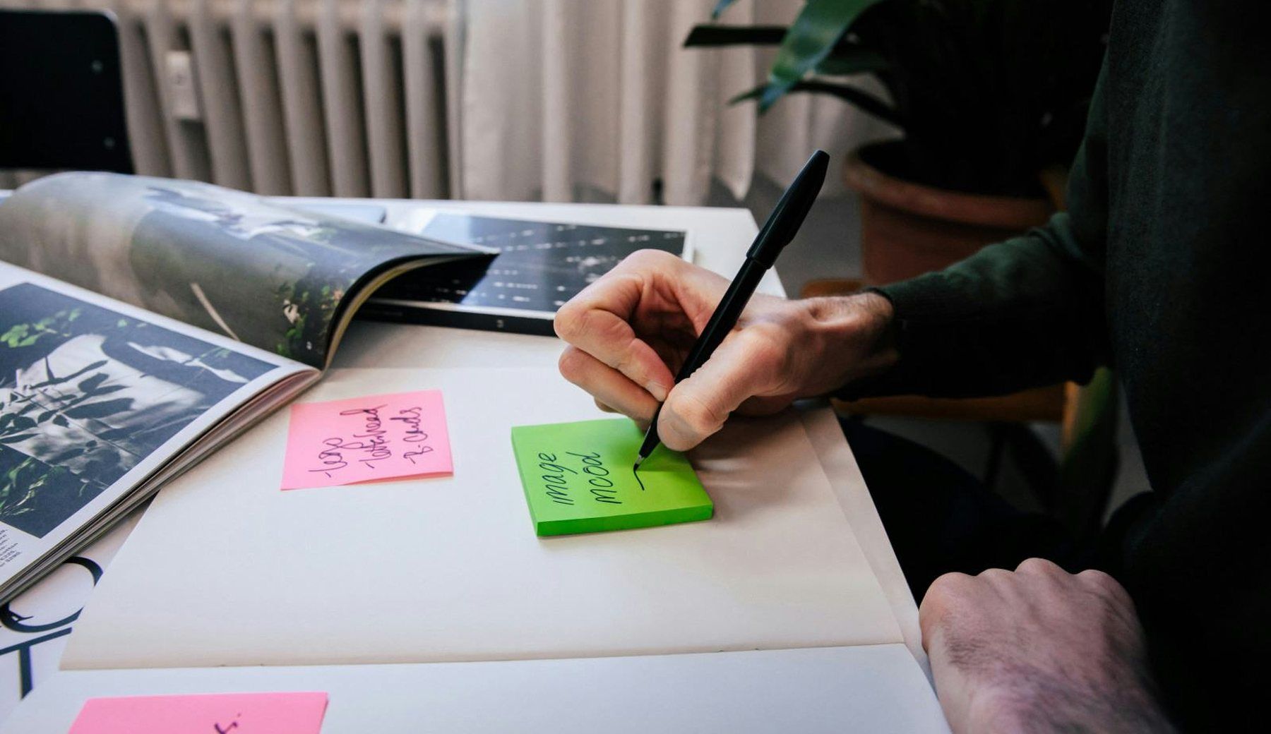A hand drawing with a marker on a large open spread, with sticky notes and printed reference pages spread across the desk.