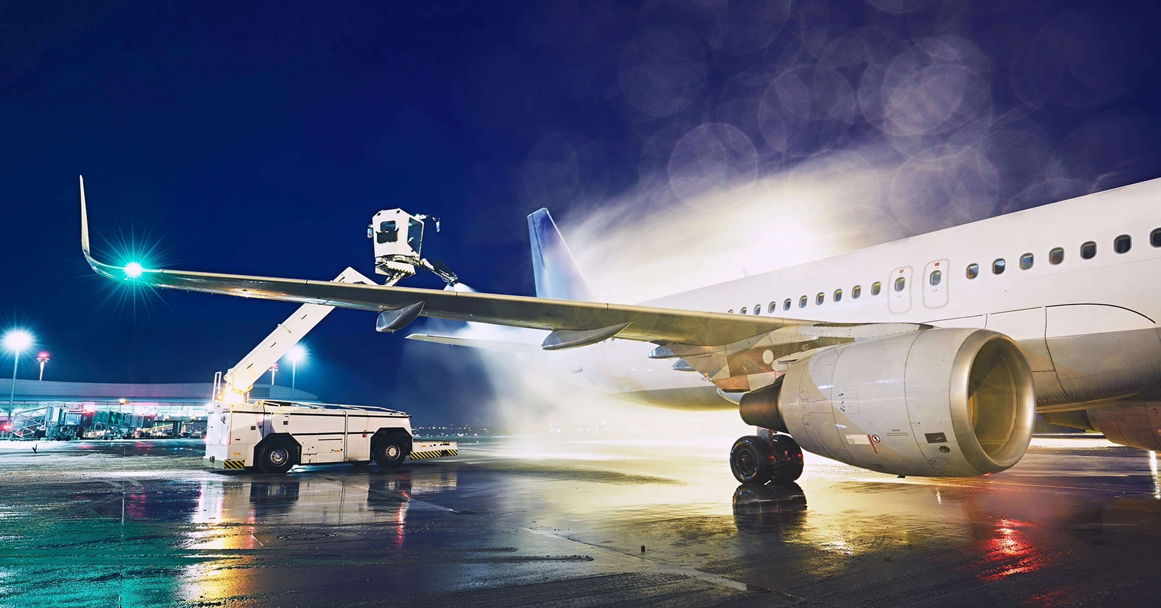 An airplane washing crane spraying water on a plane at night.