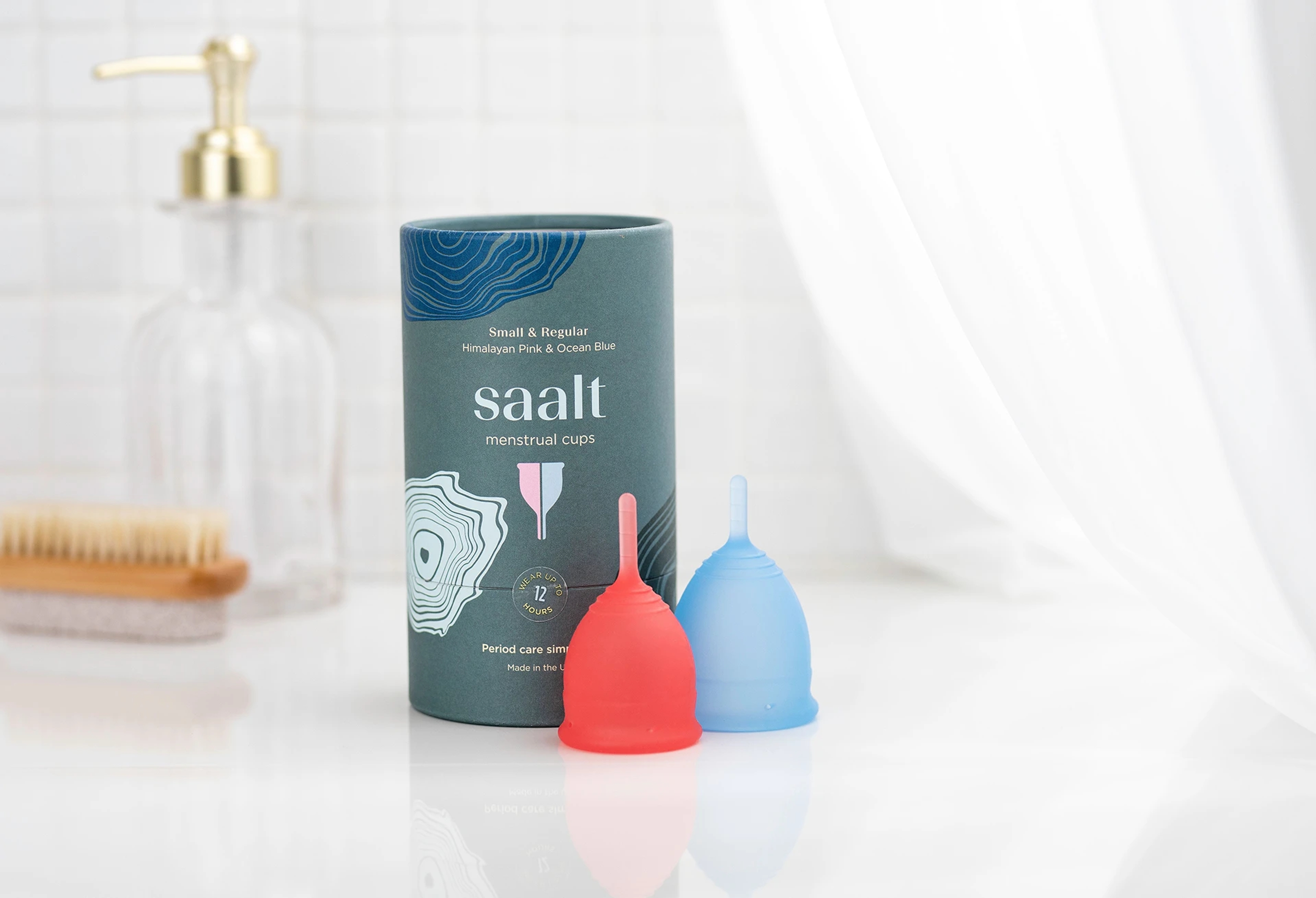 A Saalt menstrual cup package and two period cups sitting before it.