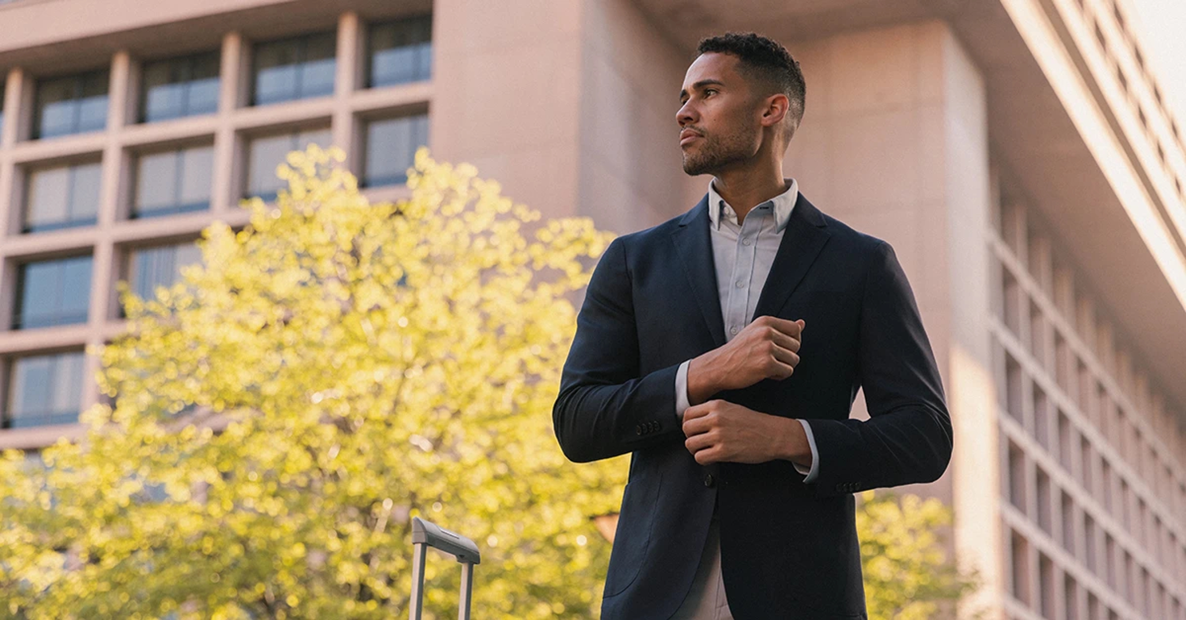 A man standing outside a building buttoning up his blazer cuffs.