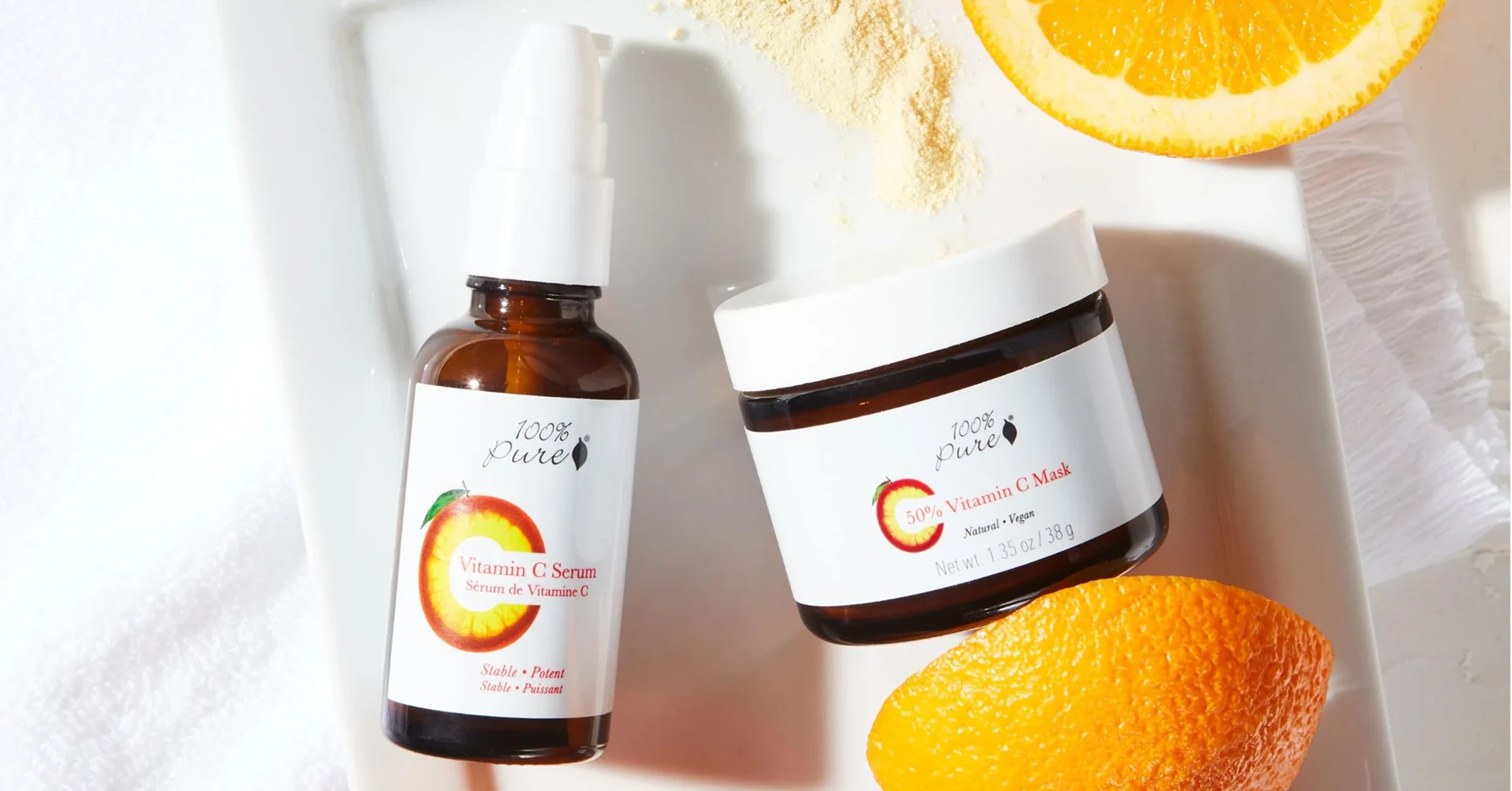 A selection of bottles of skincare products against a white surface with orange slices