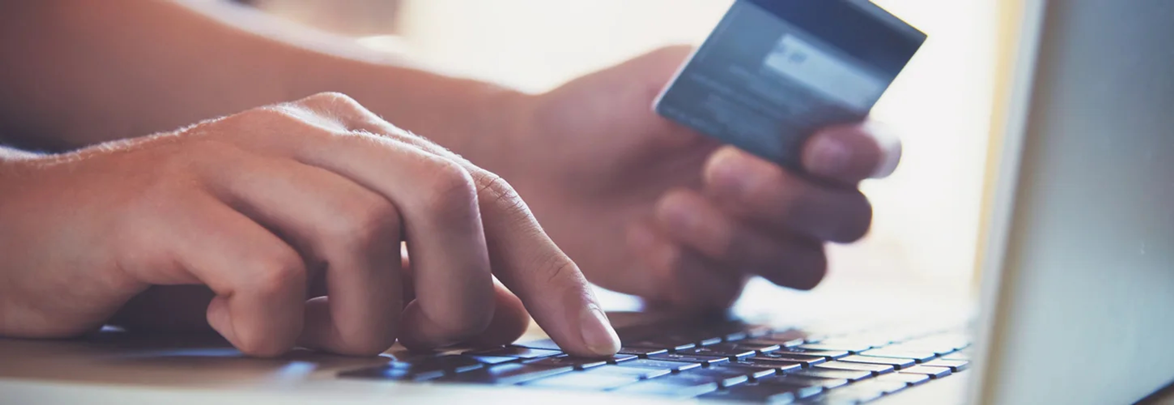 A person typing on the keyword while holding a credit card about to make a purchase