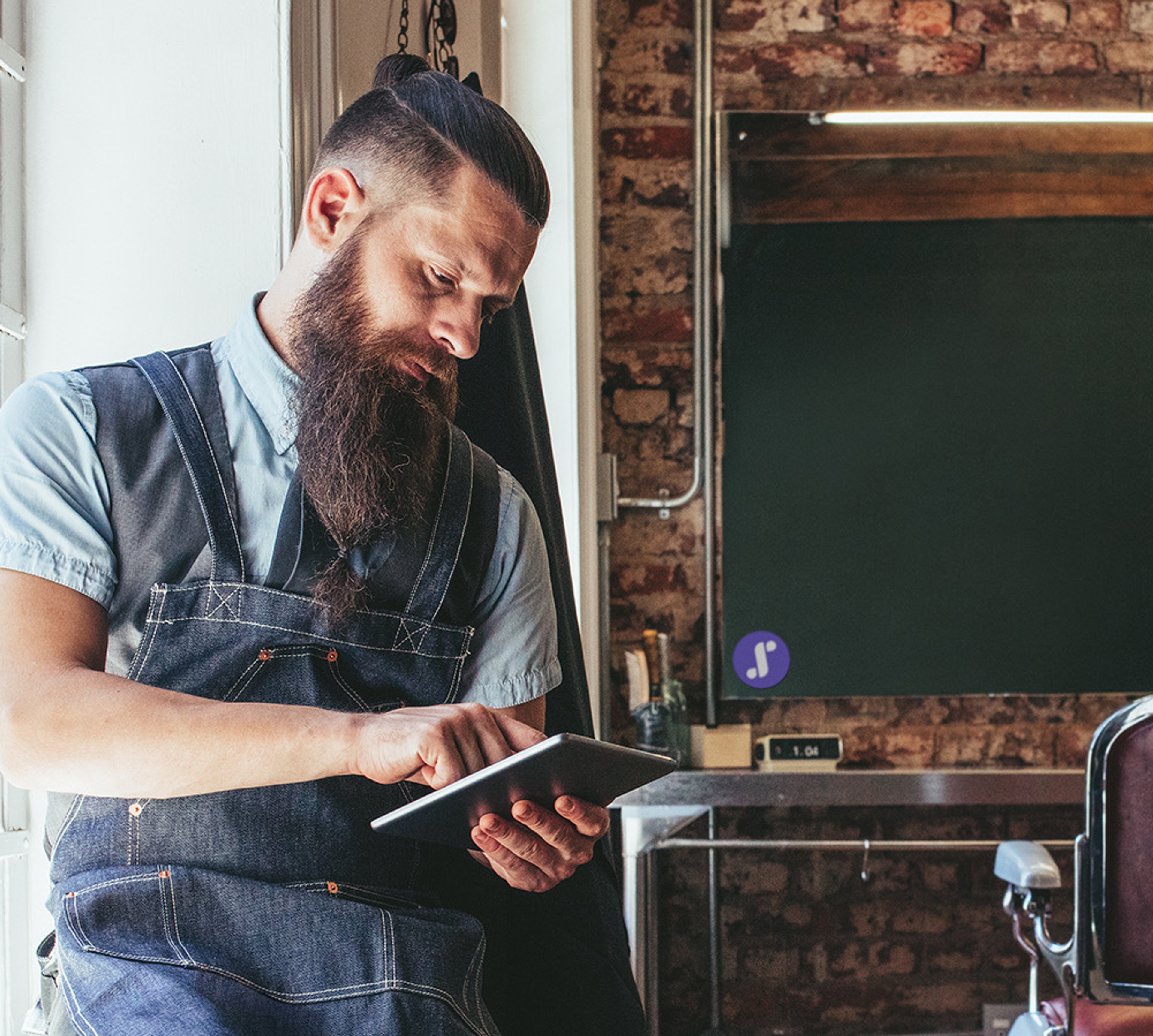 A barber working on a tablet in his shop.