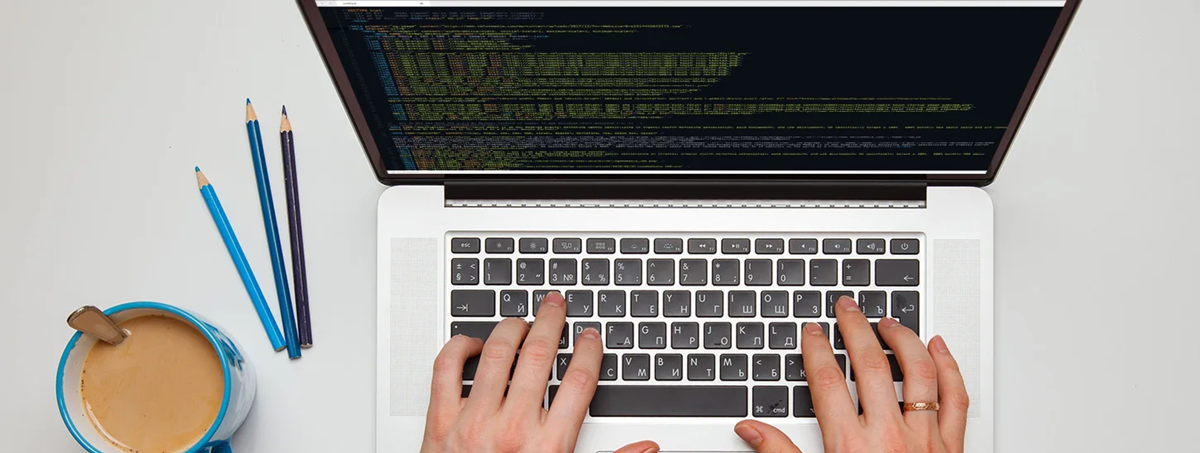 A person typing on a laptop at a desk with coffee and pencils