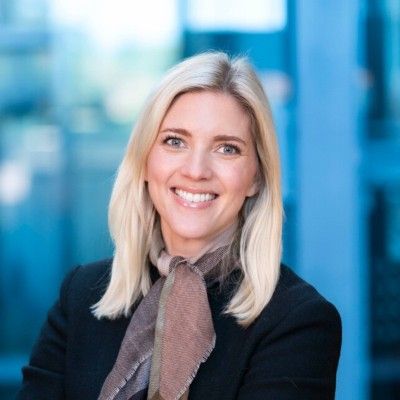 Portrett av Julie Isdahl, som smiler mot kameraet i svart blazer og mønstret skjerf.